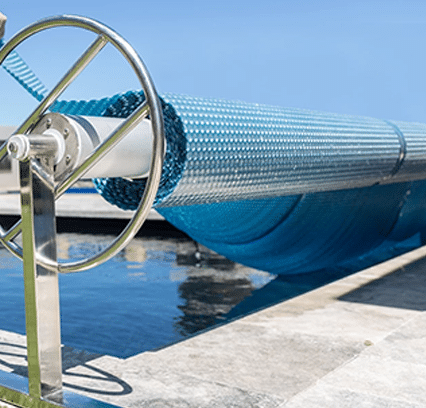 A blue rolled-up hose on a metal reel beside a concrete dock, under clear blue skies; ideal for home improvement projects. | AES - Pool Heating & Energy Efficient Products