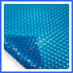 A close-up image of a blue bubble wrap sheet. The surface is covered with evenly spaced circular air pockets, creating a textured pattern. The sheet is slightly curled at one corner, revealing the individual bubbles' structure. | AES - Pool Heating & Energy Efficient Products