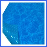 A close-up view of a blue pool cover with a bubble texture on one side. The cover is partially folded back at one corner to reveal the bubbles underneath, resembling the surface of a swimming pool. | AES - Pool Heating & Energy Efficient Products